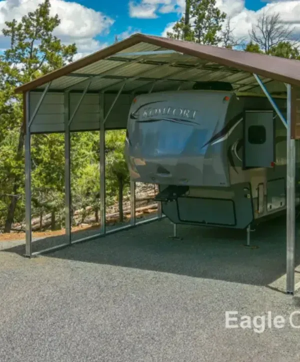 Komfort fifth wheel RV parked under a metal carport in a wooded area