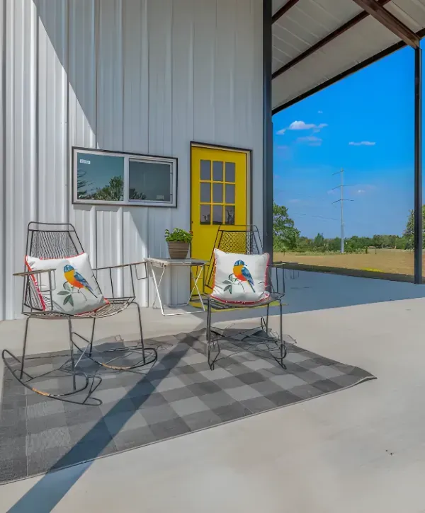 Metal building porch with yellow door and chairs on concrete patio