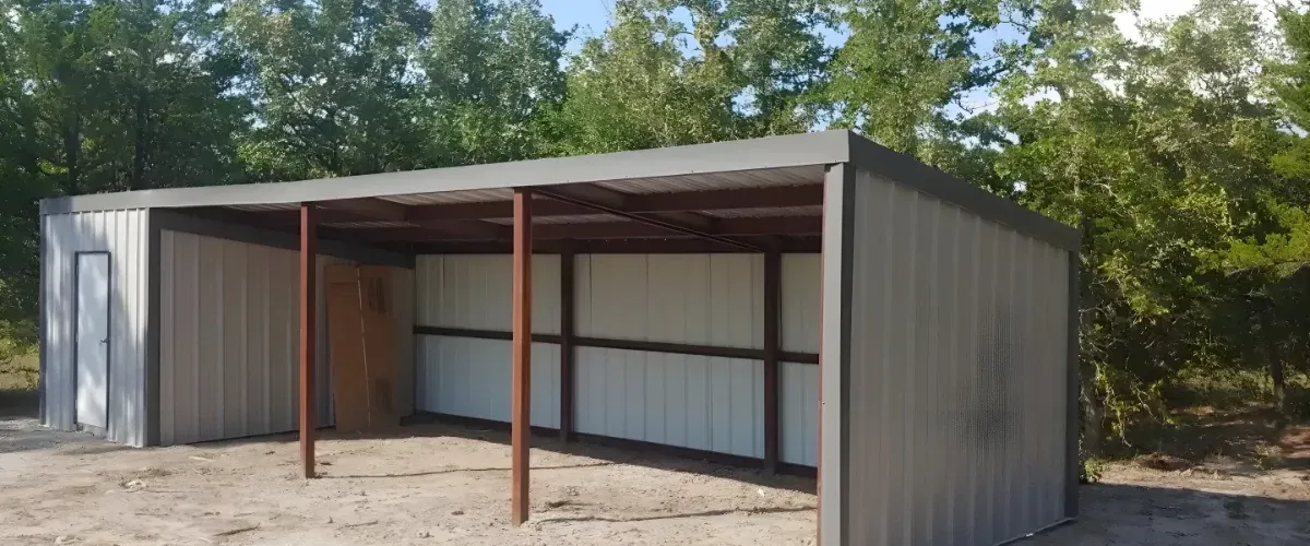 Partially completed metal storage shed with steel frame and panel walls in a wooded area.