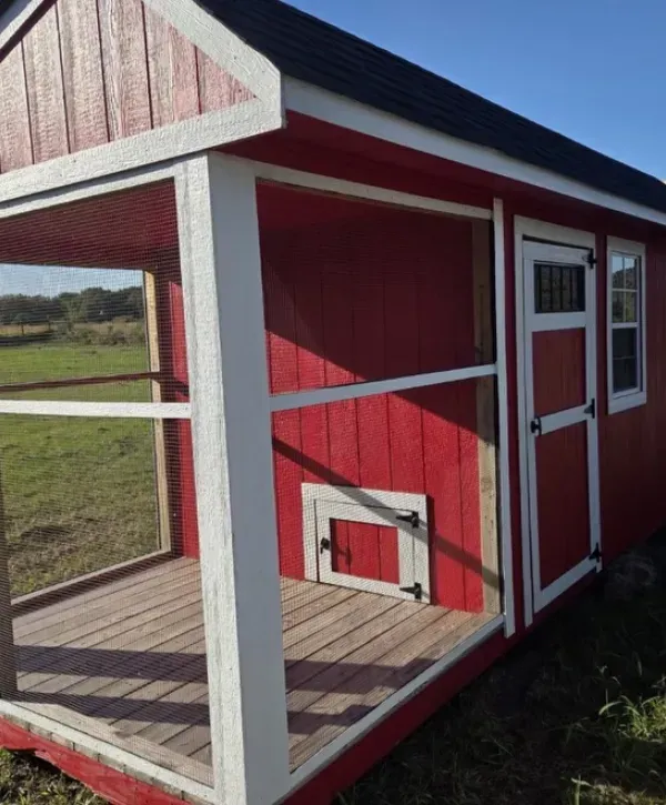 Red wooden shed with white trim and a screened porch in a grassy field