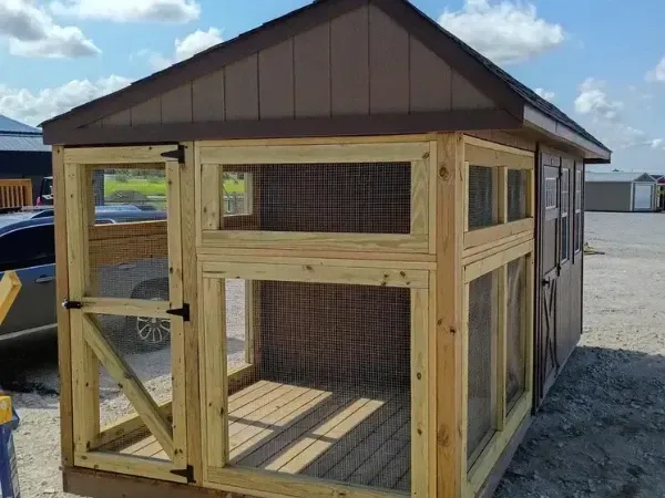 Wood-framed outdoor enclosure attached to a brown shed, featuring screened walls and a small gate.