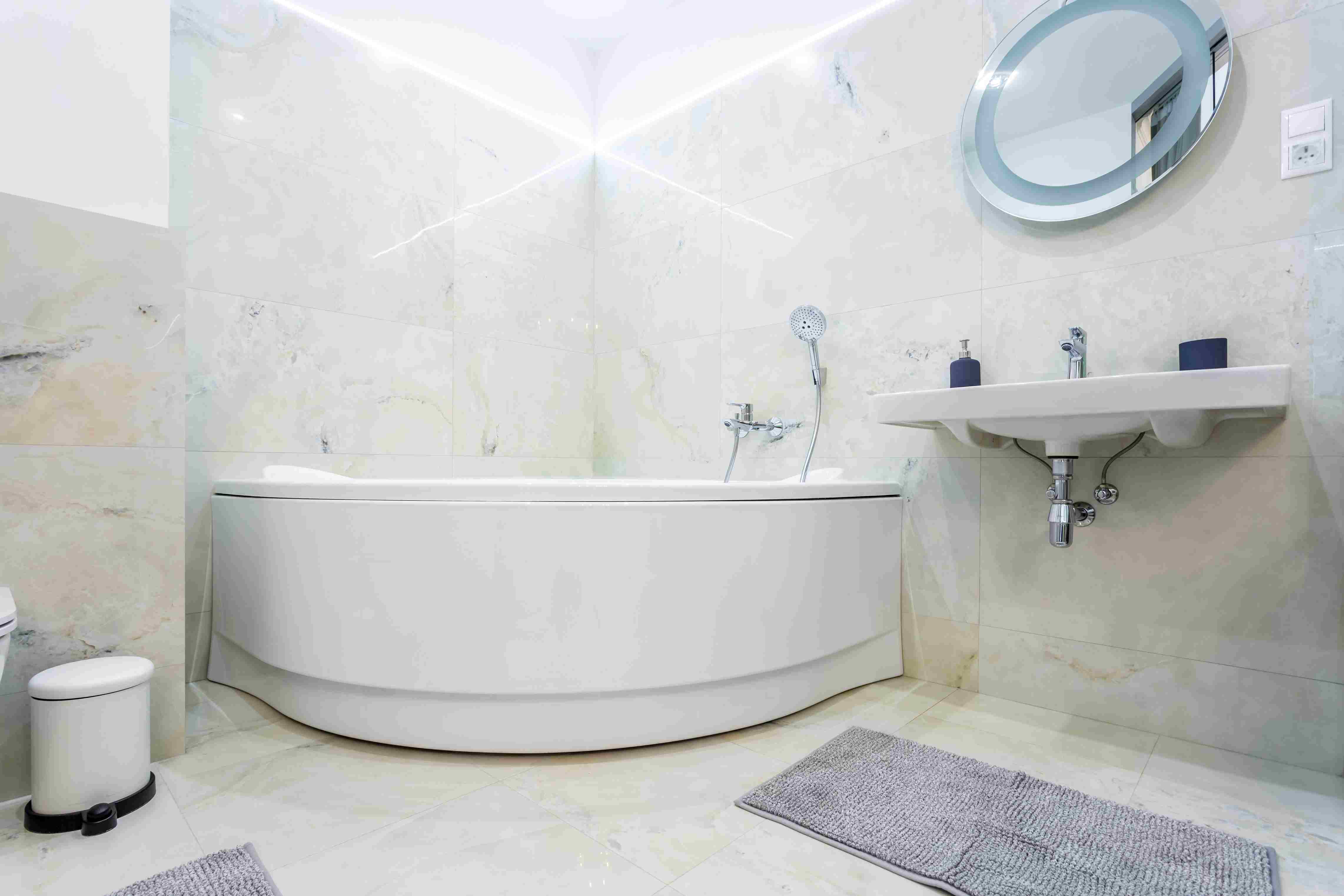 Modern bathroom renovation in St Albert with corner bathtub, wall mounted sink and marble tile walls