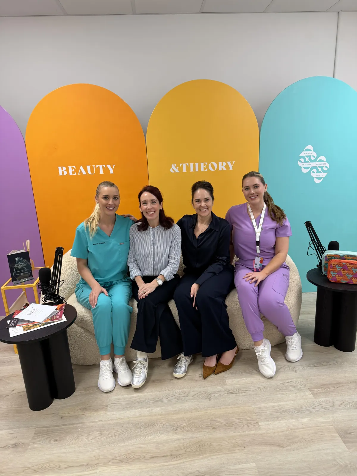 A picture of the beauty and theory team sat on the sofa with the colourful headboards behind with the skin rocks trainers
