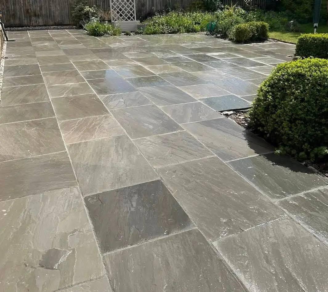 Sandstone paving with a circle feature between dark timber fences in a Manchester back garden