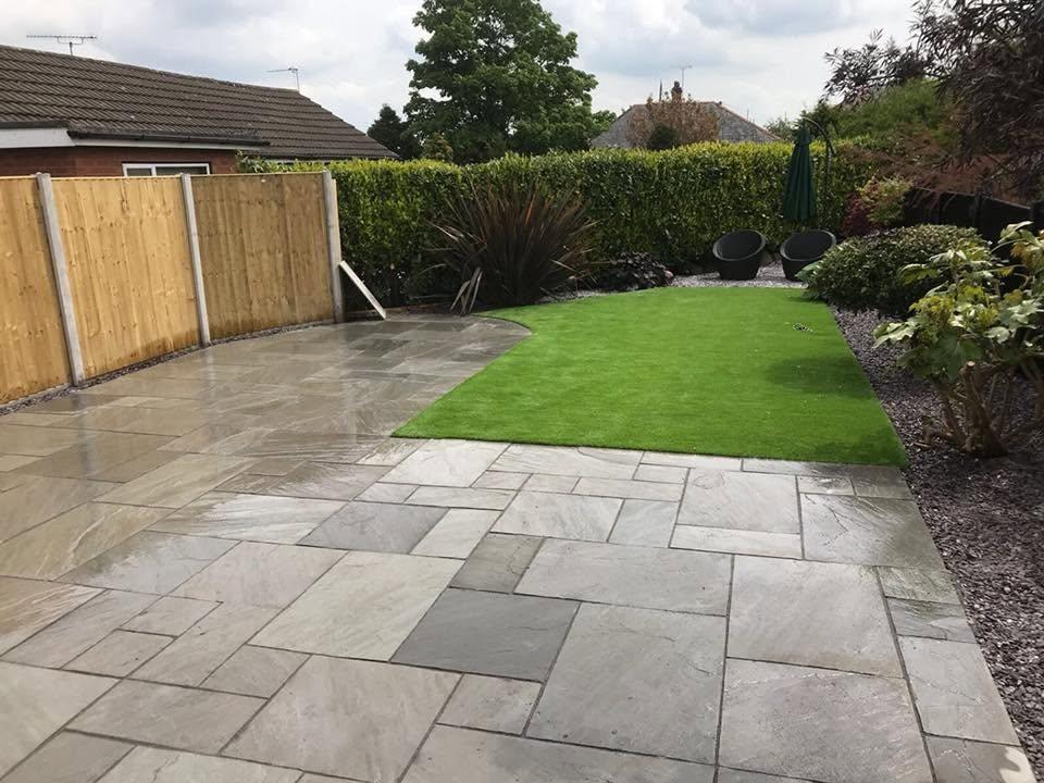 Sandstone paving with a circle feature between dark timber fences in a Manchester back garden
