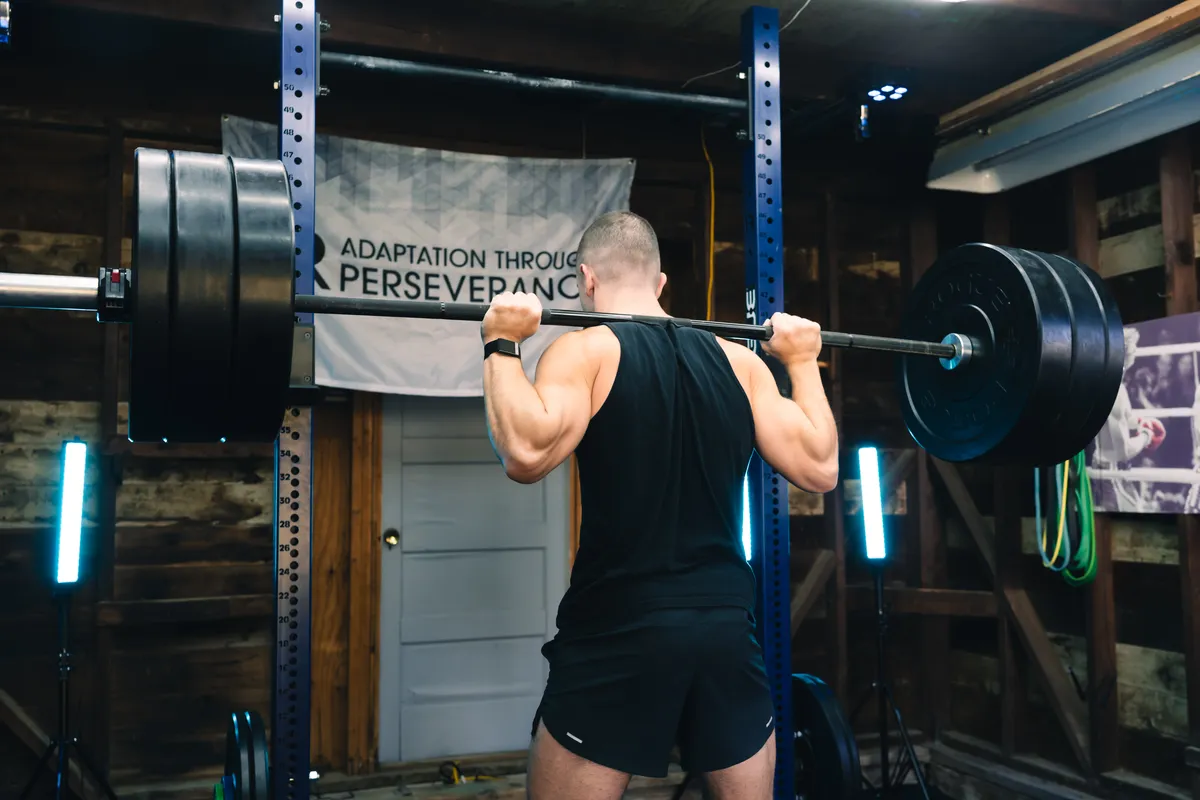 Jonathan back squatting in his home gym under the Adaptation Through Perseverance banner