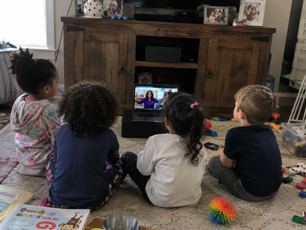 Students sit in a semicircle watching the teacher on a laptop