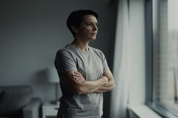 Anxiety vs overthinking difference: person standing near a window with composed but inward expression, subtle tension in stillness