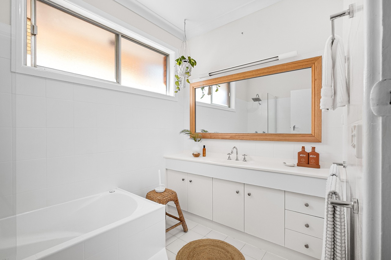 white bathroom with a wooden framed mirror, towels on the right, and a bathtub