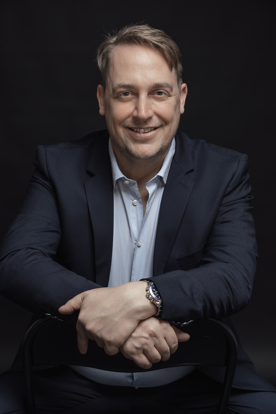 Mann sitzt auf Stuhl im Fotostudio vor schwarzem Hintergrund