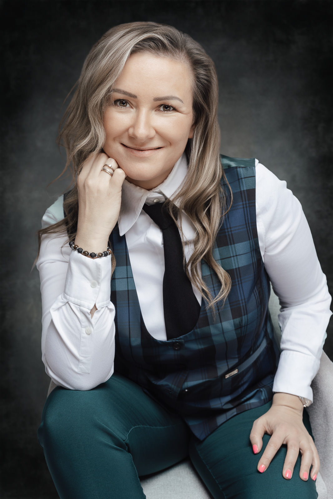 Businessportrait einer Frau mit offenem Lächeln und stilvollem Outfit vor dunklem Hintergrund