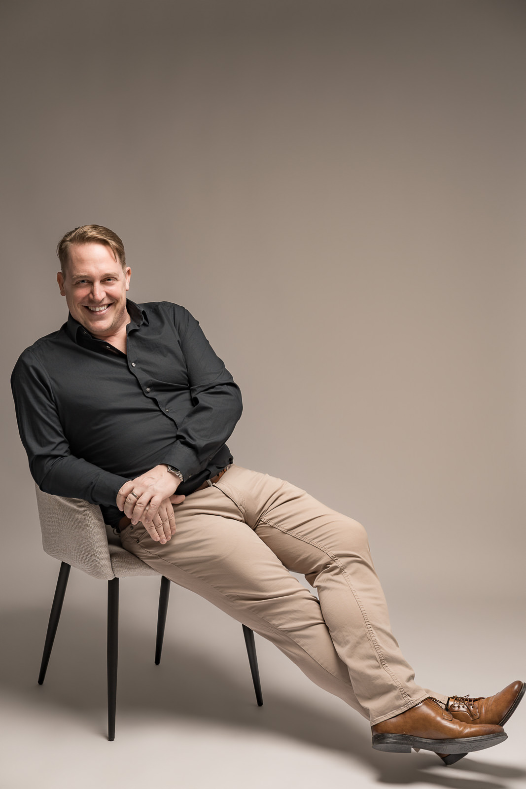 Authentisches Männerportrait mit lockerer Haltung auf Stuhl vor hellem Hintergrund