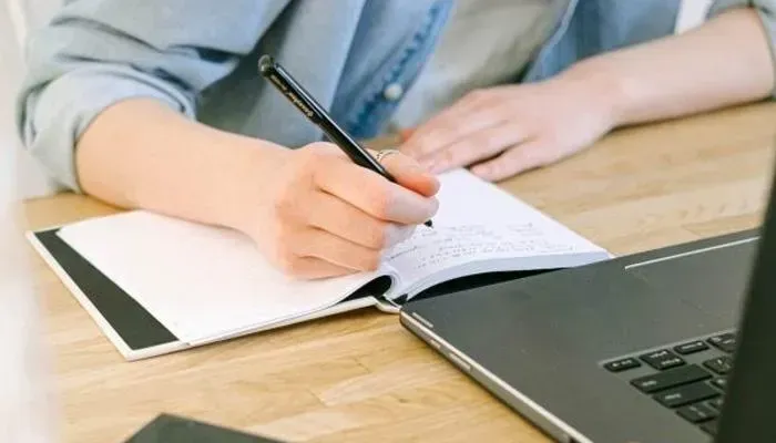 Hand writing in notebook beside laptop for content strategy