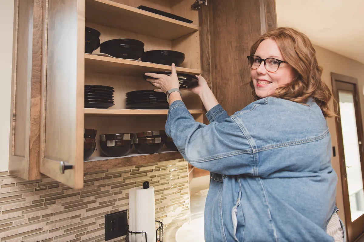 Image of Katie the owner of Organize With Kurnsie putting dishes into a cabinet