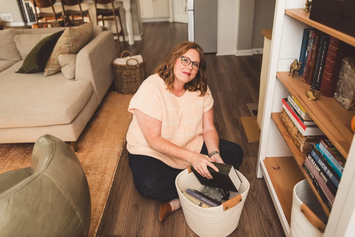 image of Katie the owne of OWK sitting on the floor in front of a bookcase, sorting books that are in a basket