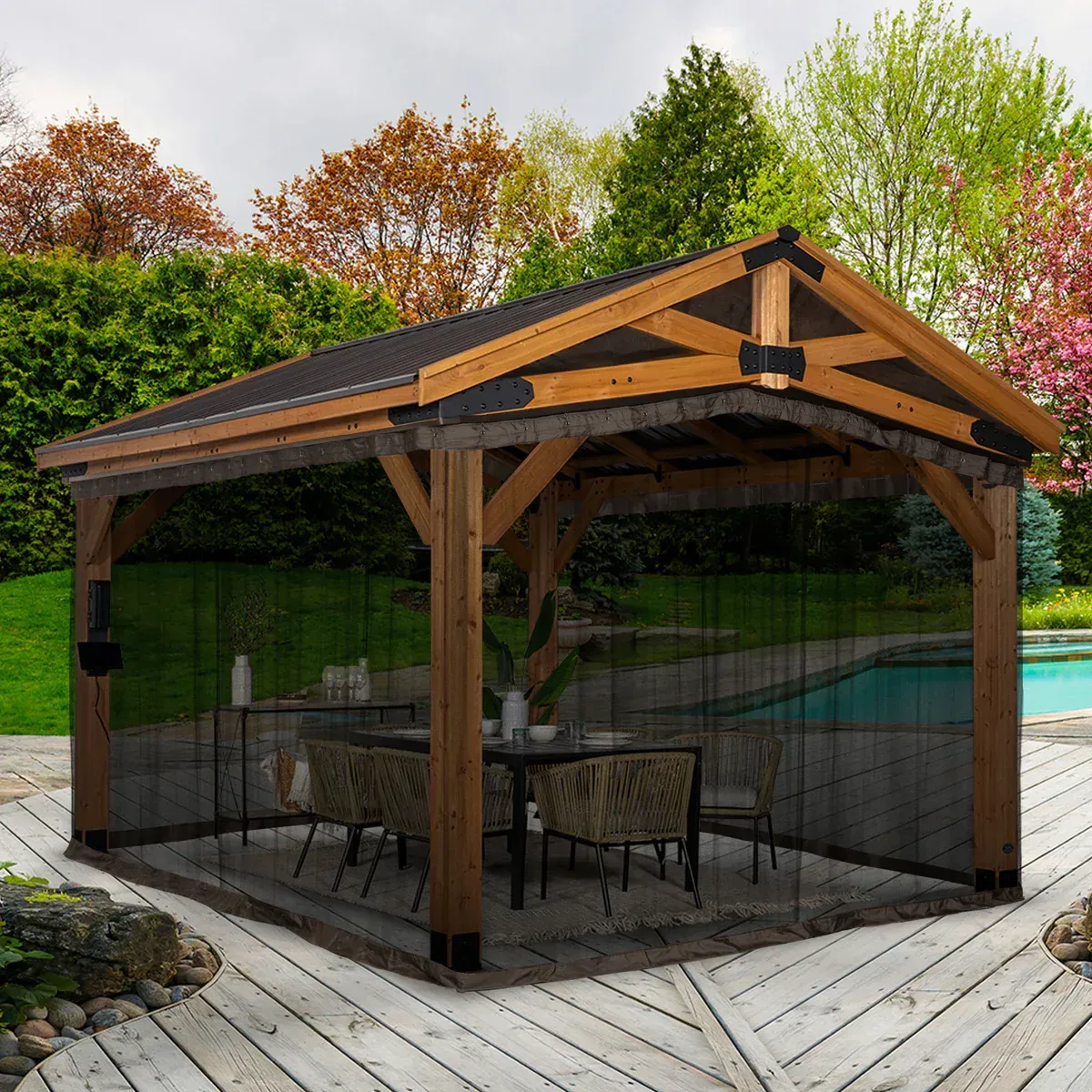 Wooden backyard gazebo with dark roof and mesh screens surrounding an outdoor dining area.