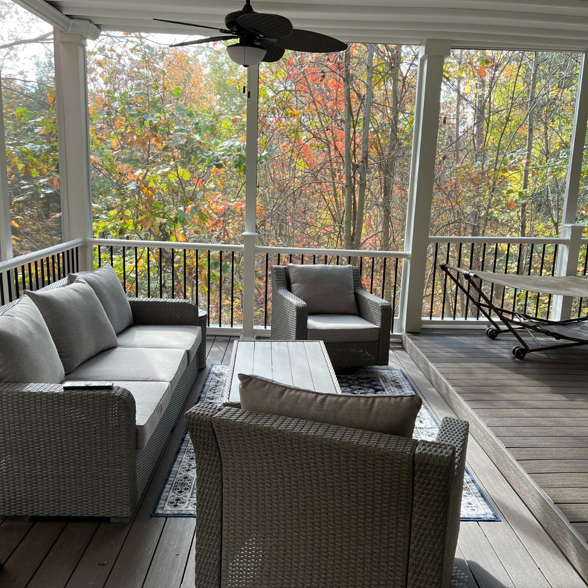 Cozy screened-in sunroom with wicker seating, ceiling fan, and views of colorful autumn trees
