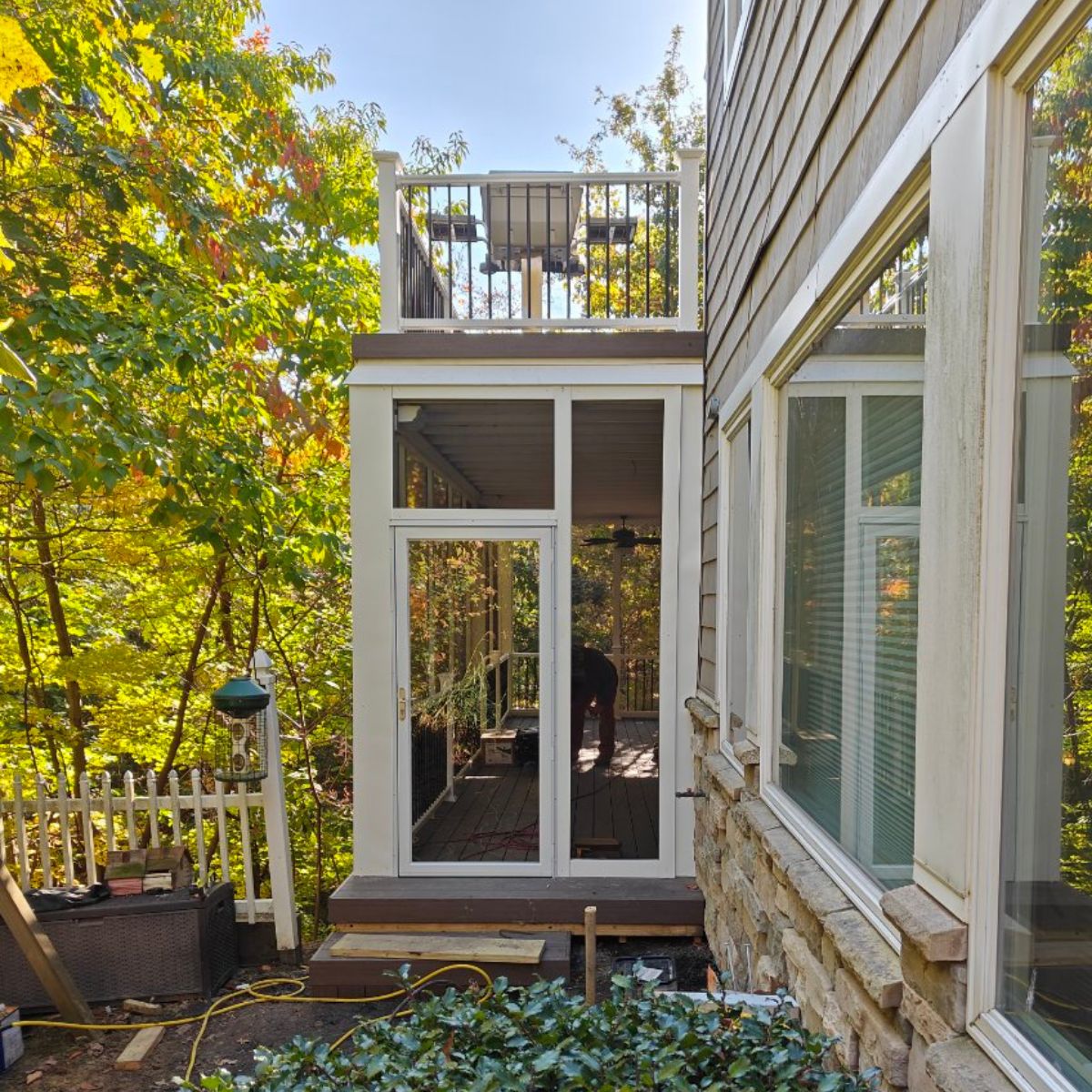 Exterior view of a modern sunroom with large glass panels and white framing attached to a home surrounded by fall foliage