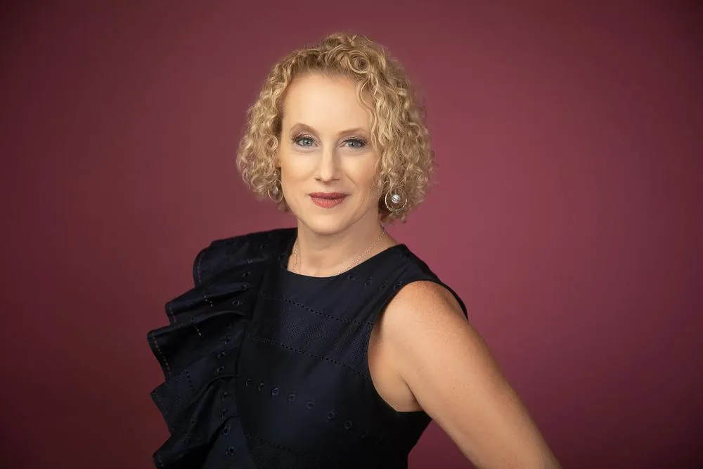 Elaine Williams is wearing a black dress with a ruffle from the right shoulder down to the waist on a red background.