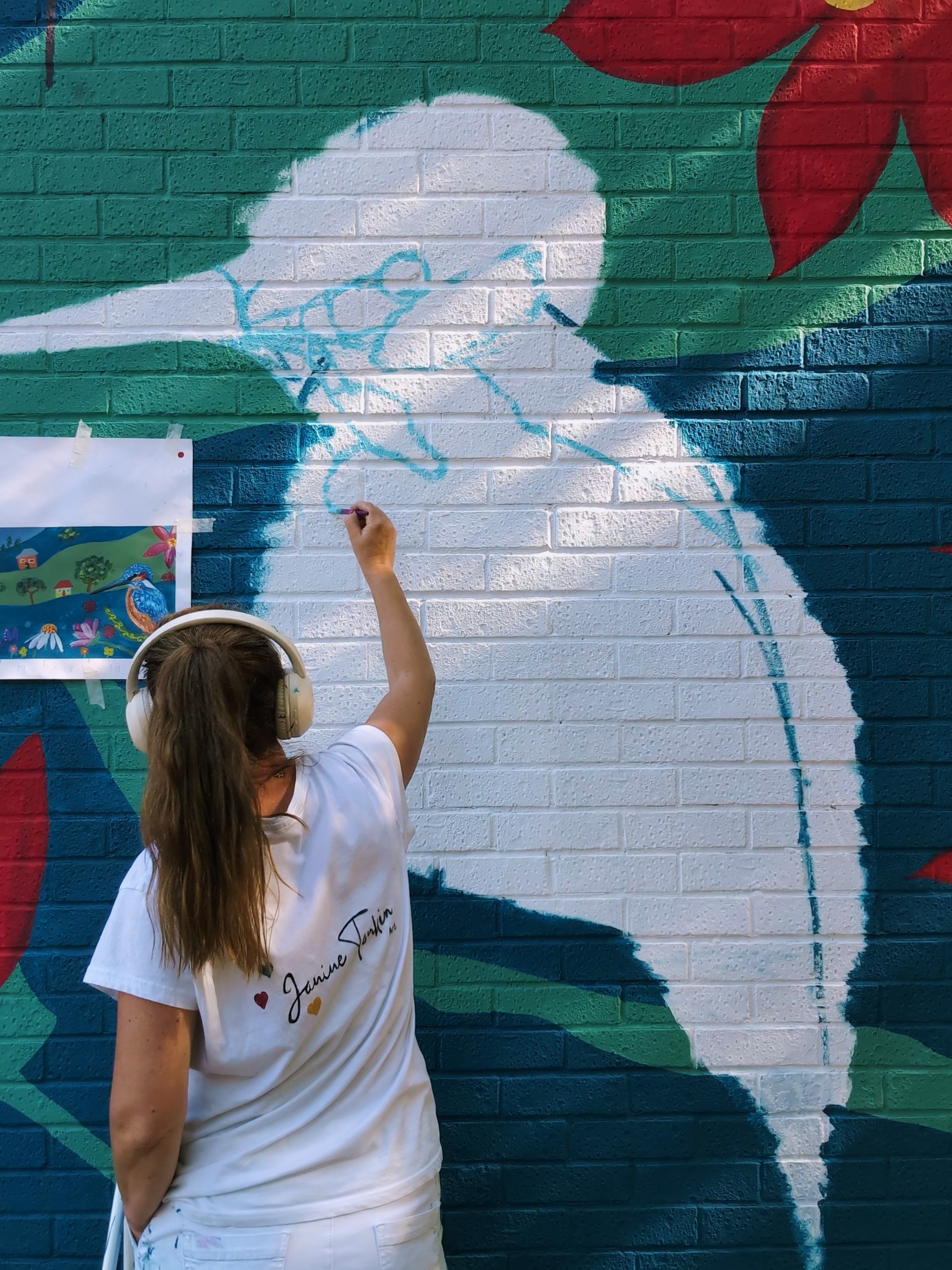 Janine Tonkin™ freehand transferring the kingfisher from her original Wild, Wonder & Bloom™ community mural design onto the Campion House wall in Bracknell. Planning and scaling the artwork by hand as part of her original community mural methodology.