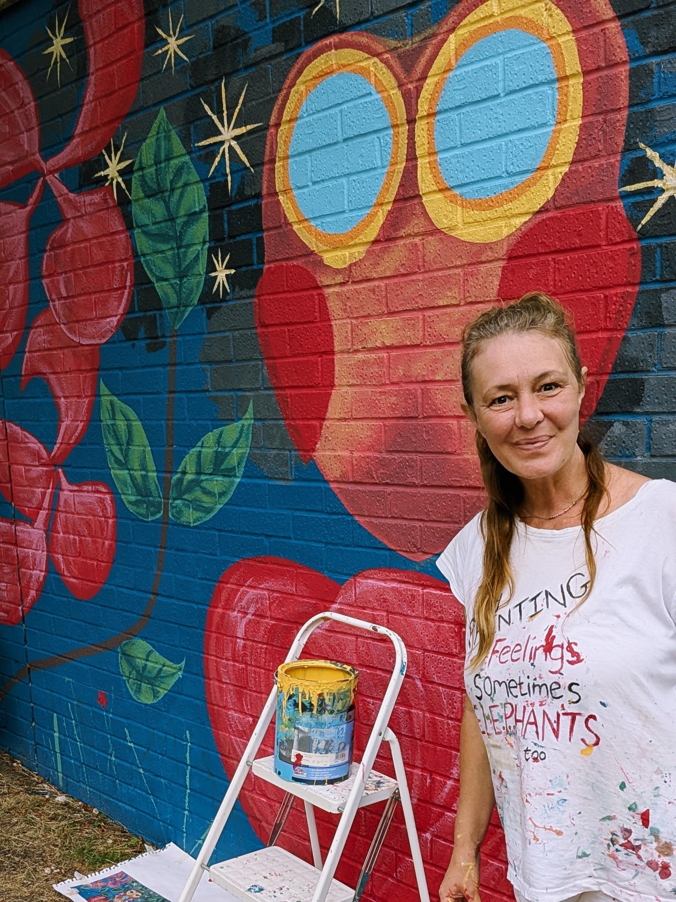 Janine Tonkin beside the owl section of the Wild and Wonderful community mural featuring stars, apples, and apple blossom inspired by resident feedback and Bracknell's historic apple orchards. 