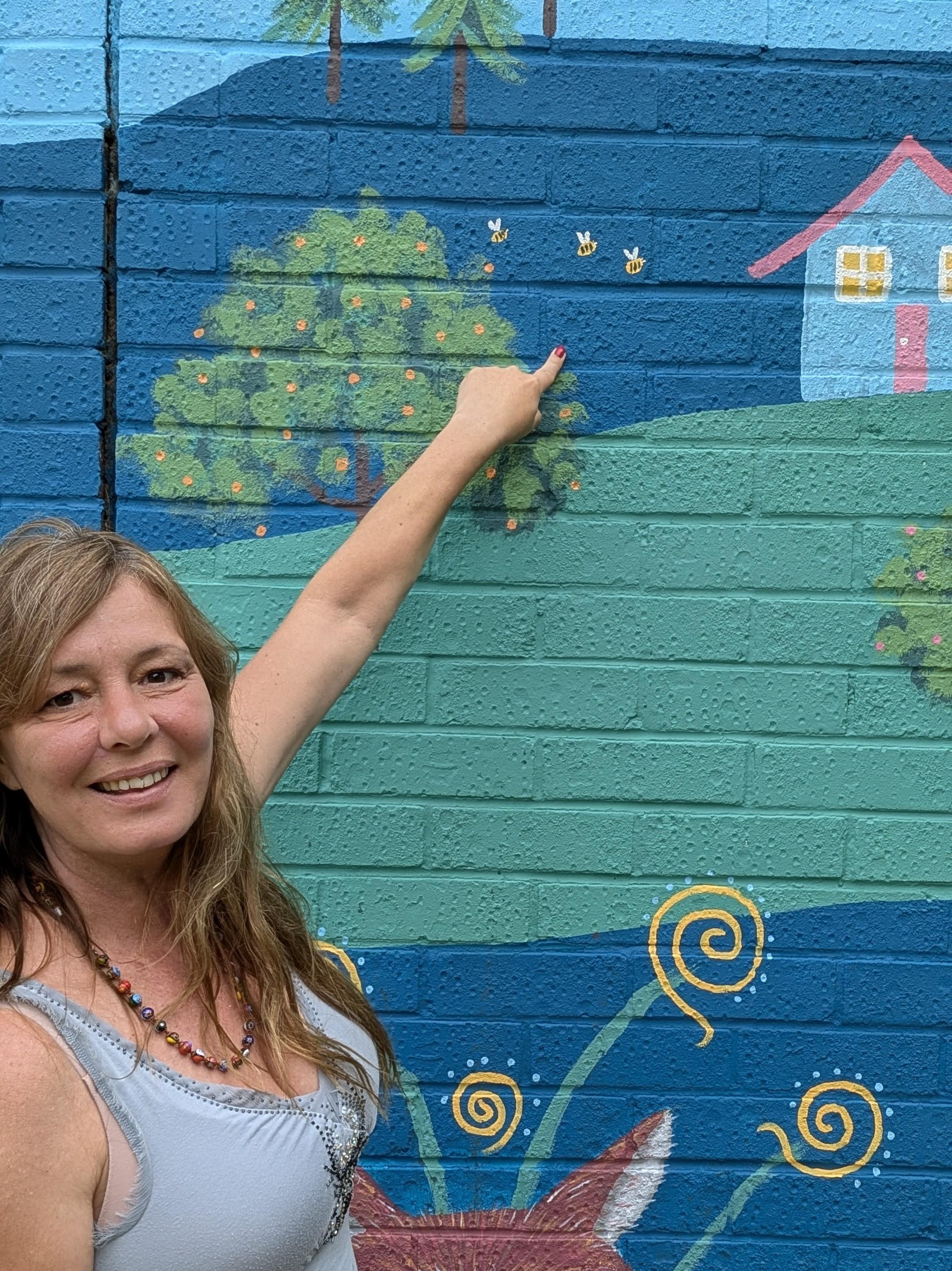 Janine Tonkin pointing to hidden bees on the Wild and Wonderful community mural at Campion House, Bracknell, inspired by resident feedback and integrated as a hidden discovery.