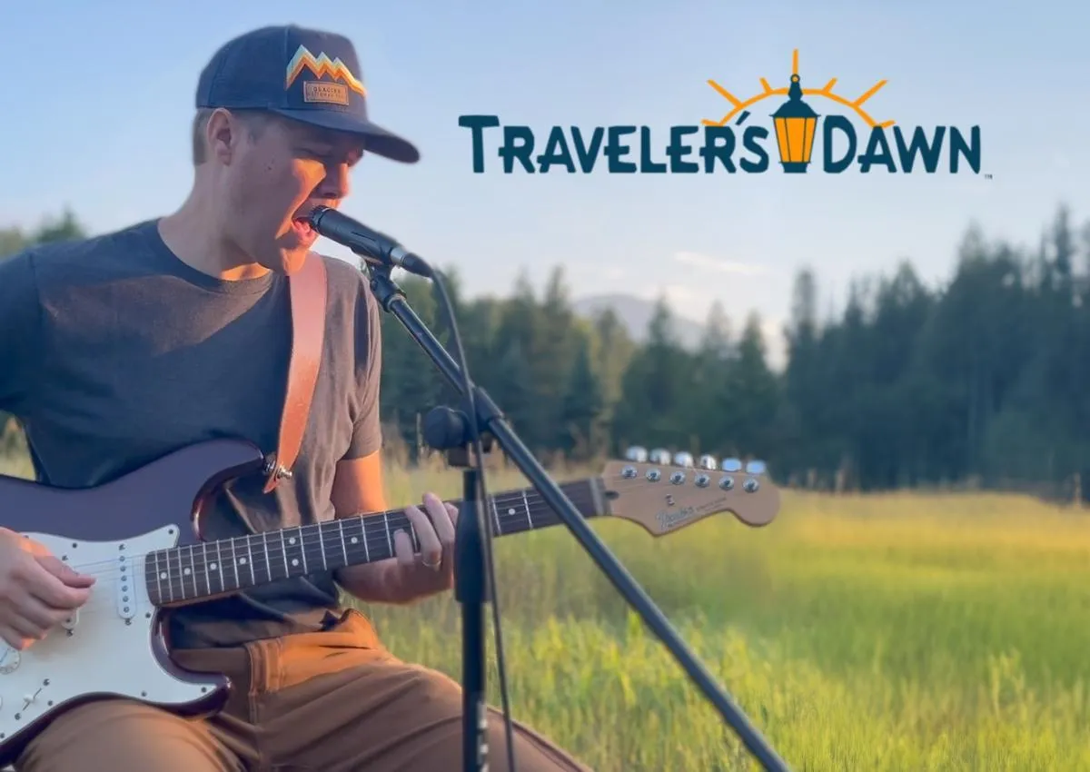 David from Traveler's Dawn playing a Fender Stratocaster electric guitar and singing into Shure SM57 microphone in front of a backdrop of the Rocky Mountains of Montana at sunset