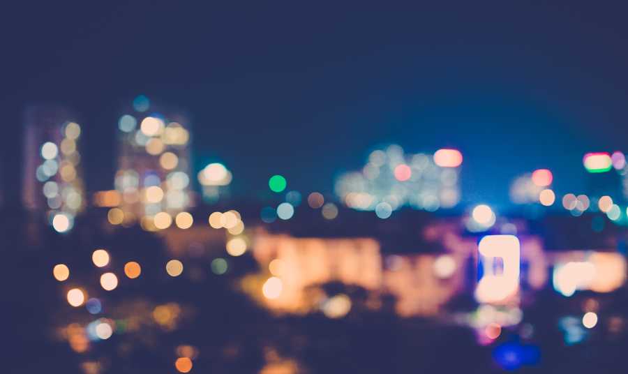 Blurred city skyline at night with colorful lights, symbolizing uncertainty, transition, and new beginnings.