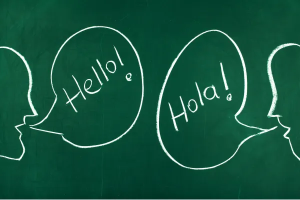 Chalkboard with speech bubbles showing “Hello!” and “Hola!” in English and Spanish.
