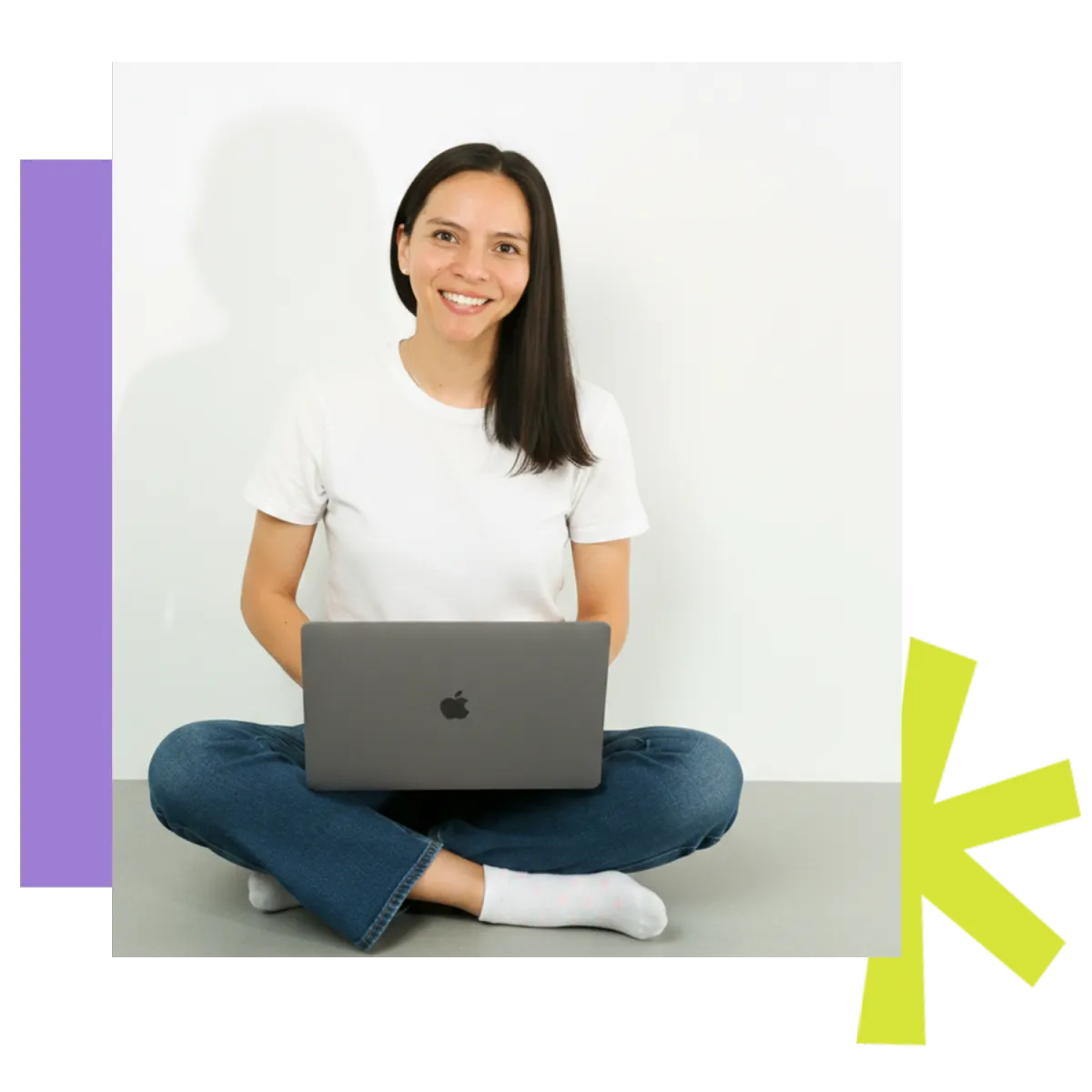 A woman with dark hair, wearing a white t-shirt and jeans, smiling and sitting cross-legged while holding a laptop on her lap. Beside her are abstract geometric shapes in purple and bright green.