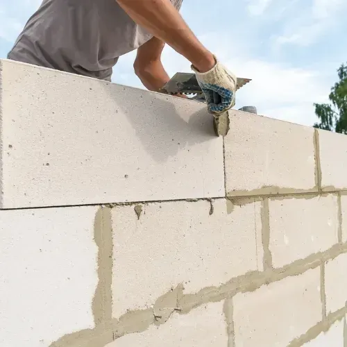 Masonry contractor applying mortar to stone blocks in Sugar Land, TX.