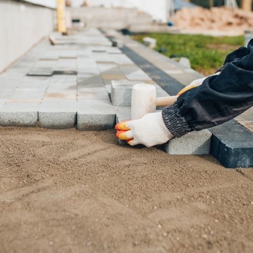 Paver installation in Sugar Land, TX, with worker setting stone pavers and using a rubber mallet.