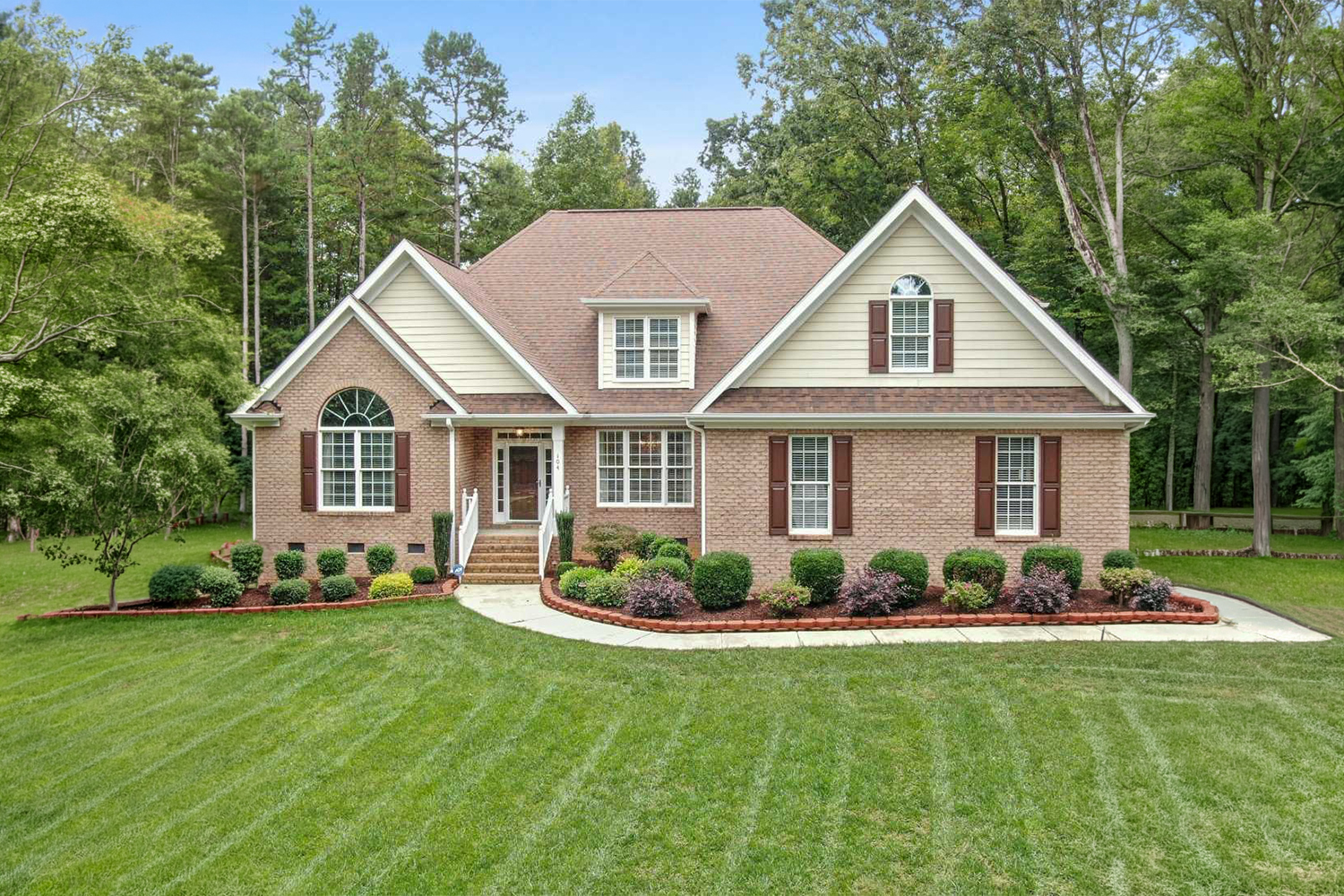 Curved stamped concrete walkway bordered by freshly mulched flower beds, colorful landscaping, and a well-maintained green lawn.