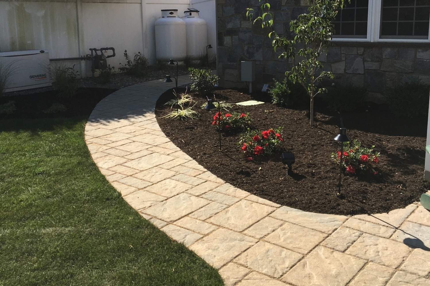 Curved stamped concrete walkway bordered by freshly mulched flower beds, colorful landscaping, and a well-maintained green lawn.
