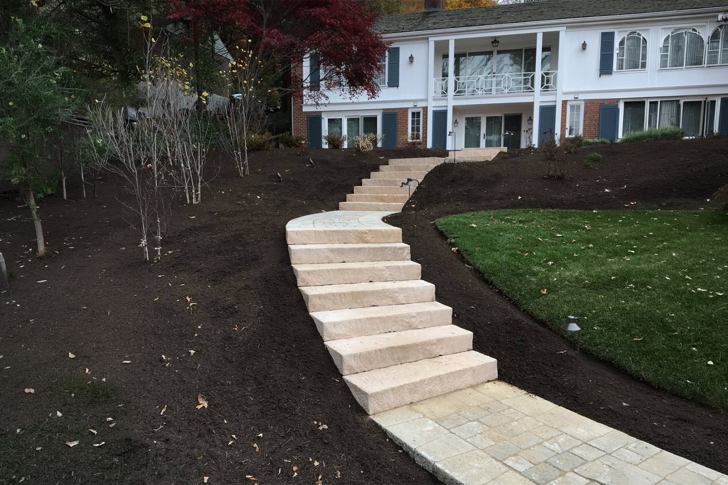 Curved stamped concrete walkway bordered by freshly mulched flower beds, colorful landscaping, and a well-maintained green lawn.