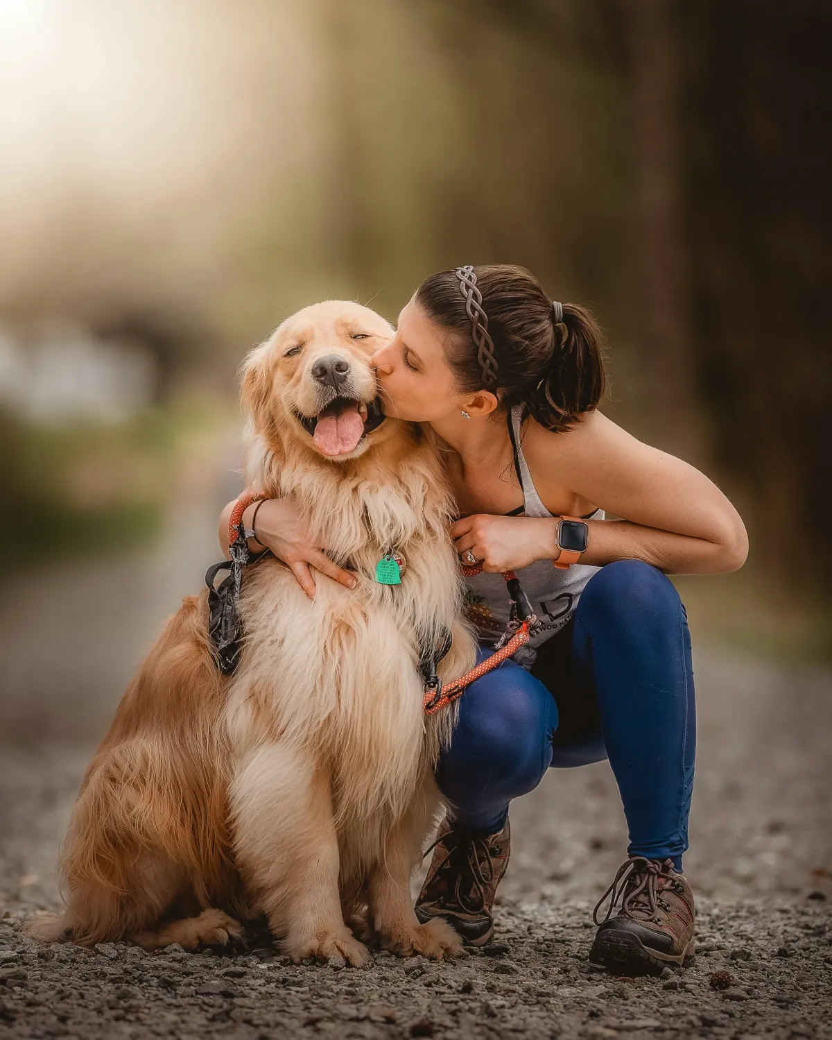 Golden Retriever dog sitting next to owner smiling, owner kissing dog