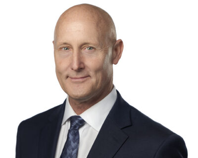 Portrait of Jordan Keane, CFA®, CAIA®, Chief Investment Officer, mid-40s male in charcoal suit and light blue shirt, three-quarter pose, neutral backdrop.