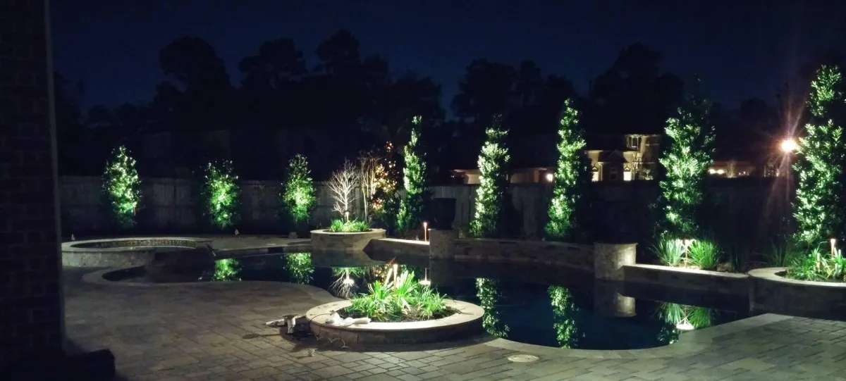 Modern backyard landscape lighting with warm LED path lights and up-lighting on trees in Houston, TX.