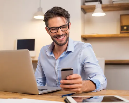 man in front of laptop smiling at phone