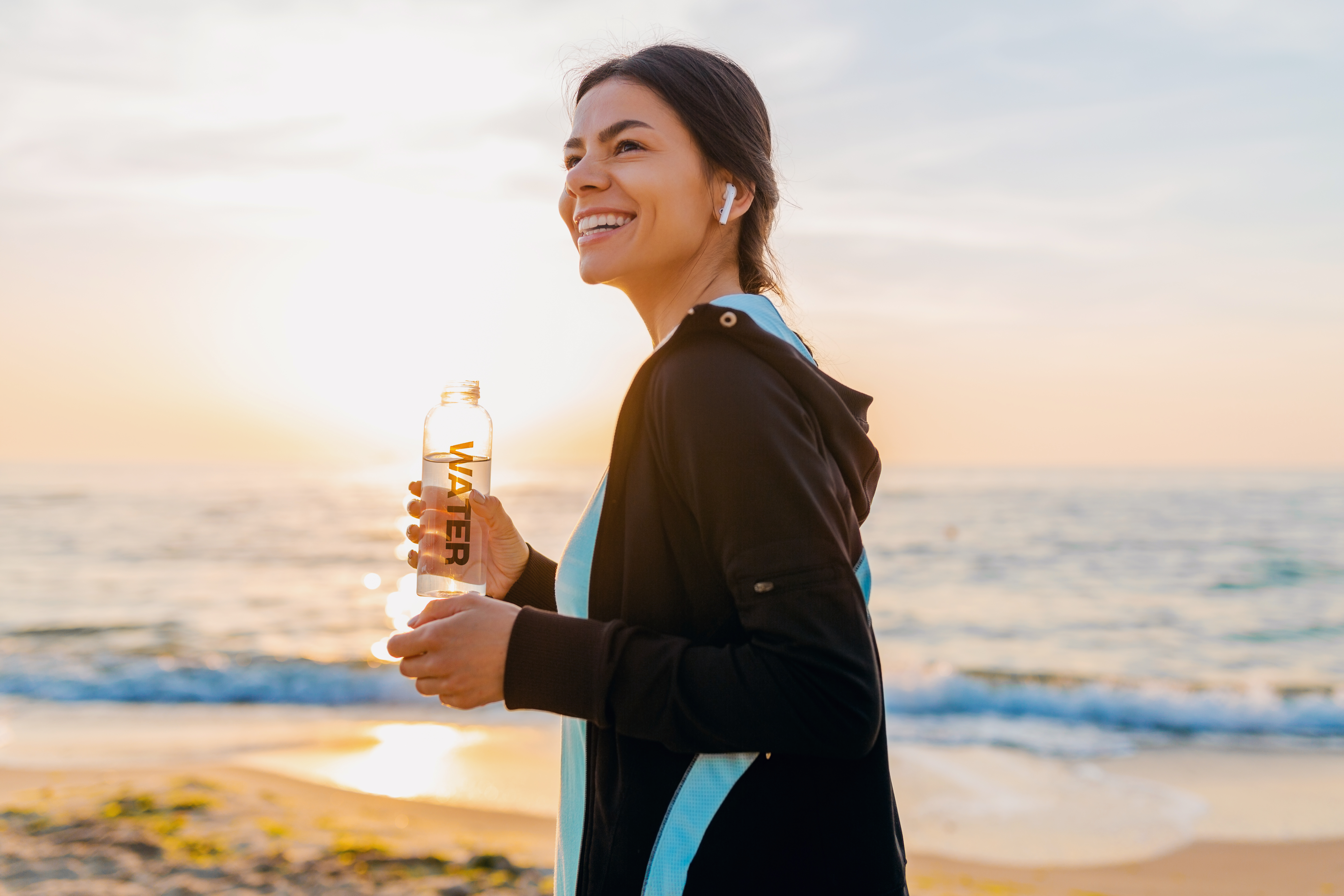 attractive-slim-woman-doing-sport-exercises-morning-sunrise-beach-sports-wear-thirsty-drinking-water-bottle-healthy-lifestyle-listening-music-wireless-earphones-smiling-happy