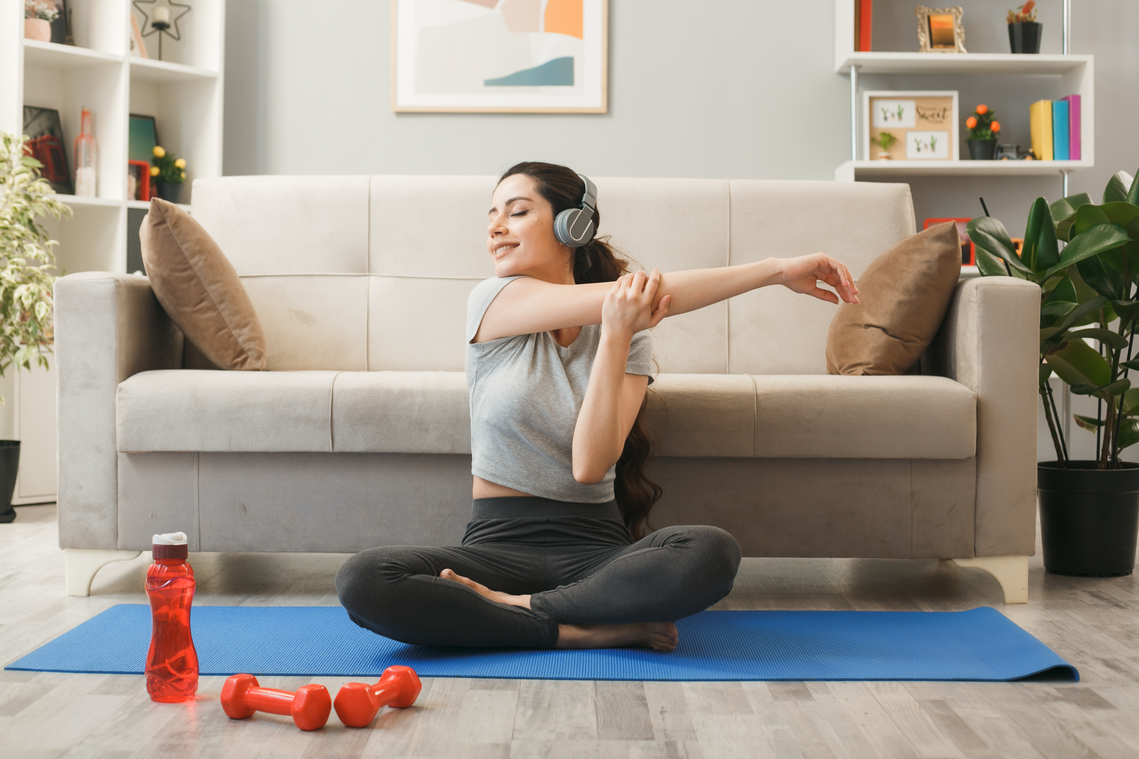 smiling with closed eyes young girl wearing headphones exercising yoga mat front sofa living room