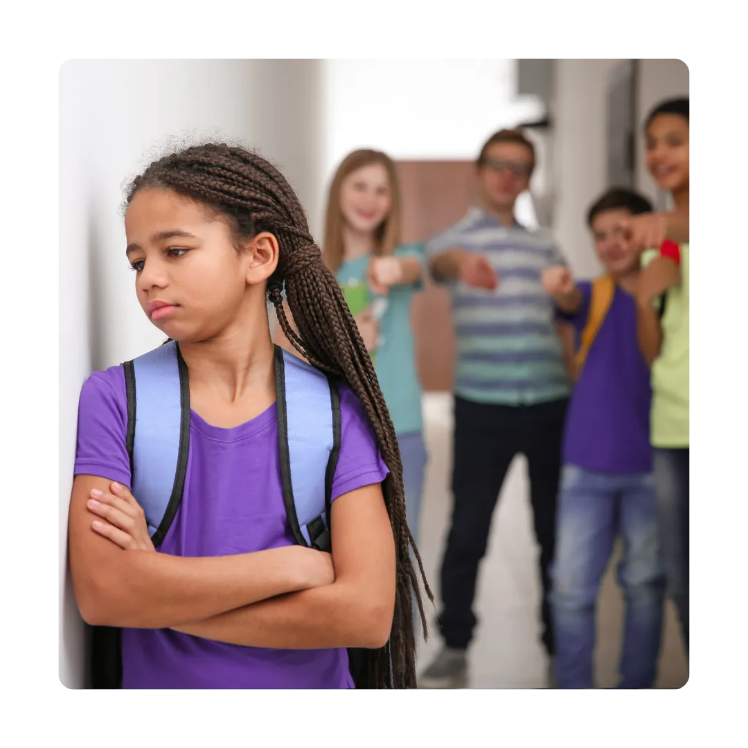 Girl leaning against a wall looking sad because because being bullied by friends behind her