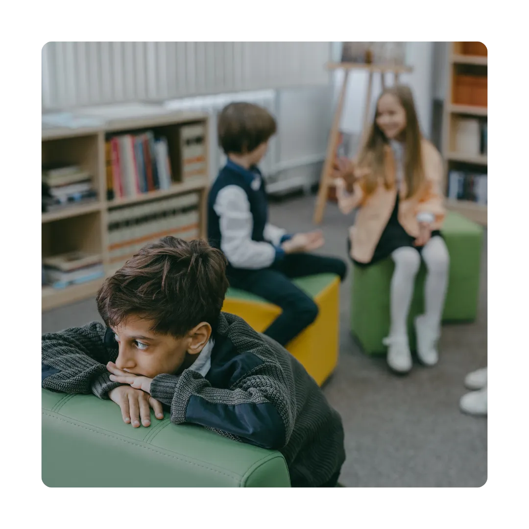 sad boy sitting by himself while kids laugh and chat behind him