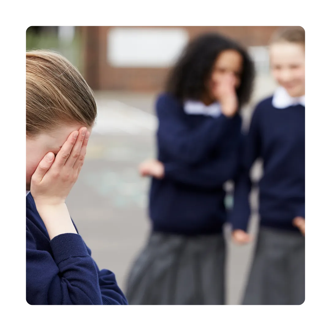 girl crying with hands over her eyes while two girls stand nearby whispering to each other about her.