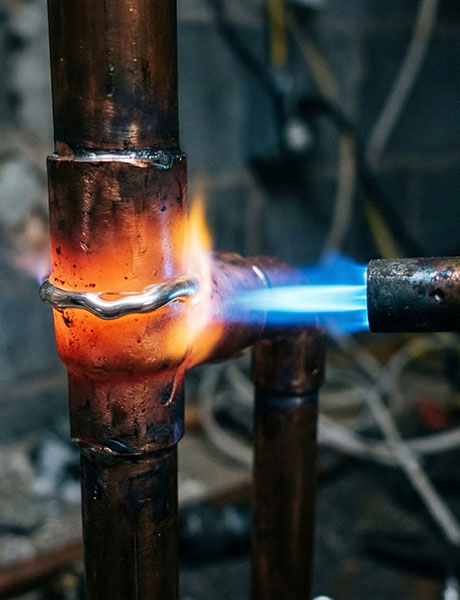 Propane torch brazing a copper pipe joint during a heating system installation