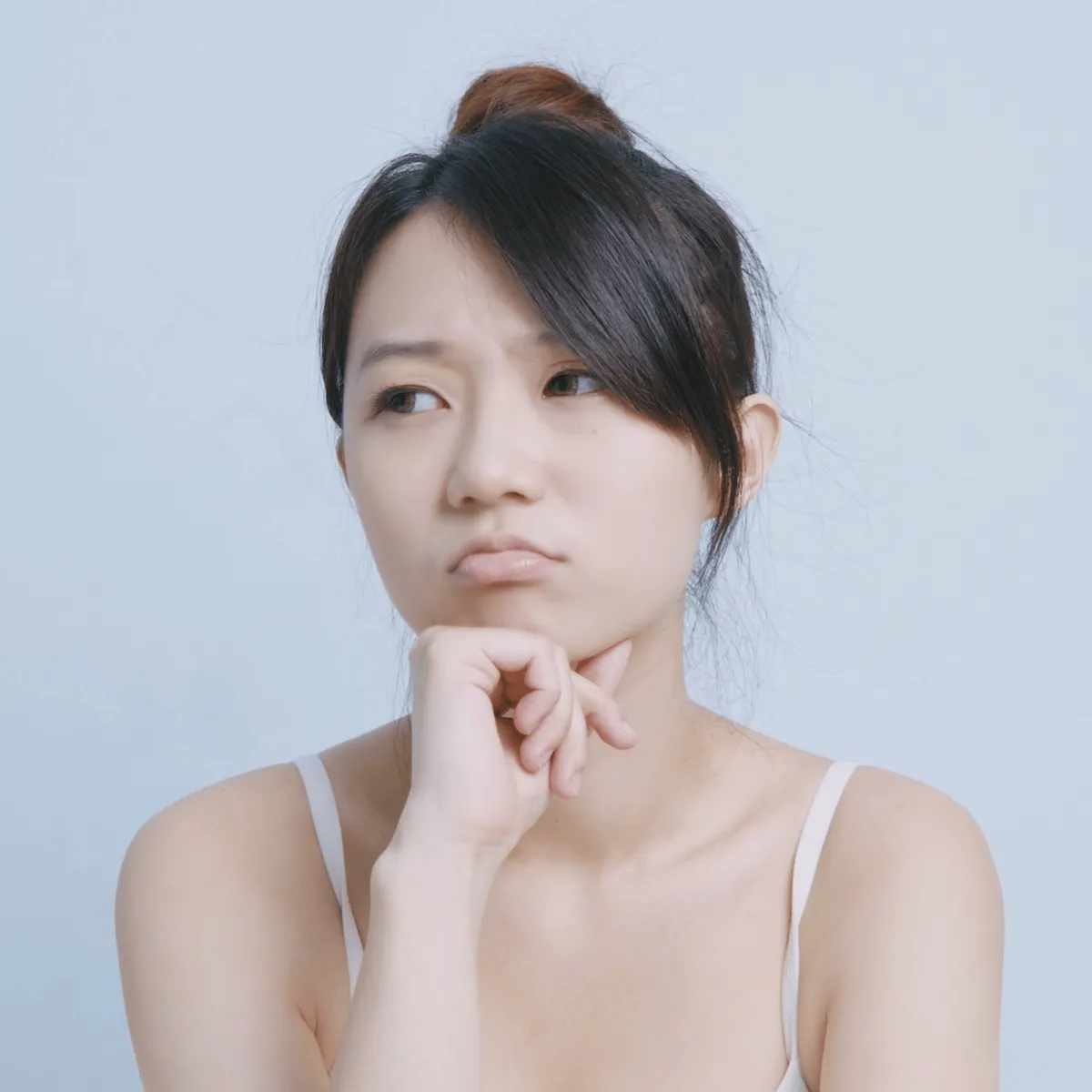 A young woman with a thoughtful and slightly frustrated expression, resting her chin on her hand while looking away.