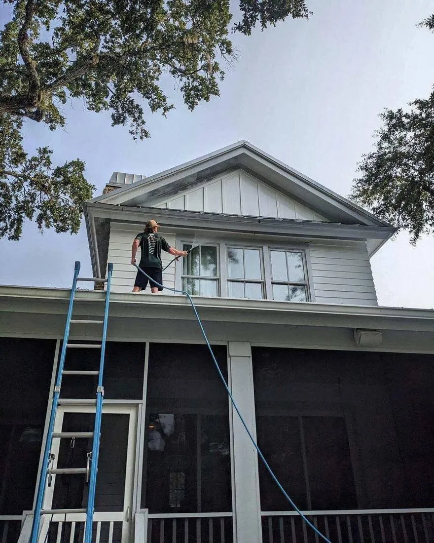 Technician soft washing the upper siding and dormer of a home in Brunswick, GA