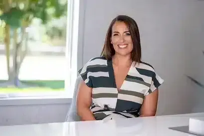 Portrait of Alex Rivera, a Latino man in his 30s, wearing a green sweater and glasses, standing in front of a softly lit holiday wreath. He looks approachable and energetic.