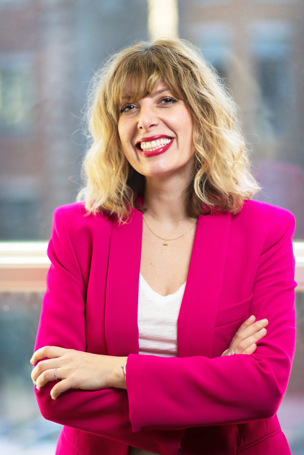 Portrait of Alex Rivera, a Latino man in his 30s, wearing a green sweater and glasses, standing in front of a softly lit holiday wreath. He looks approachable and energetic.