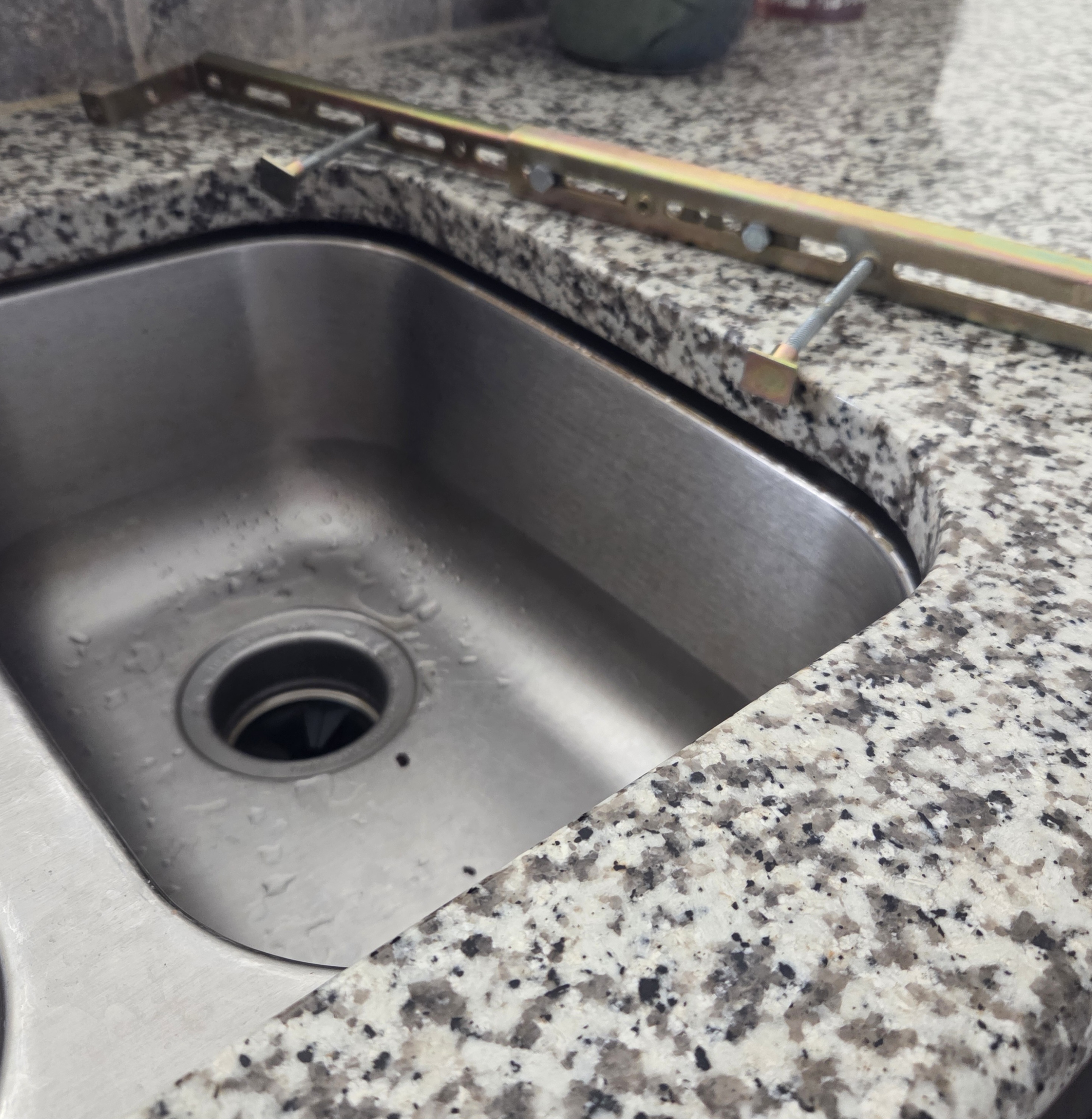 Stainless steel kitchen sink being installed with mounting clips under a granite countertop